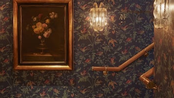 A staircase with a floral wallpaper, a framed painting of flowers, and wall-mounted lighting fixtures.