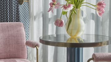 Une pièce avec une table ronde, une chaise rose et un vase rempli de fleurs.