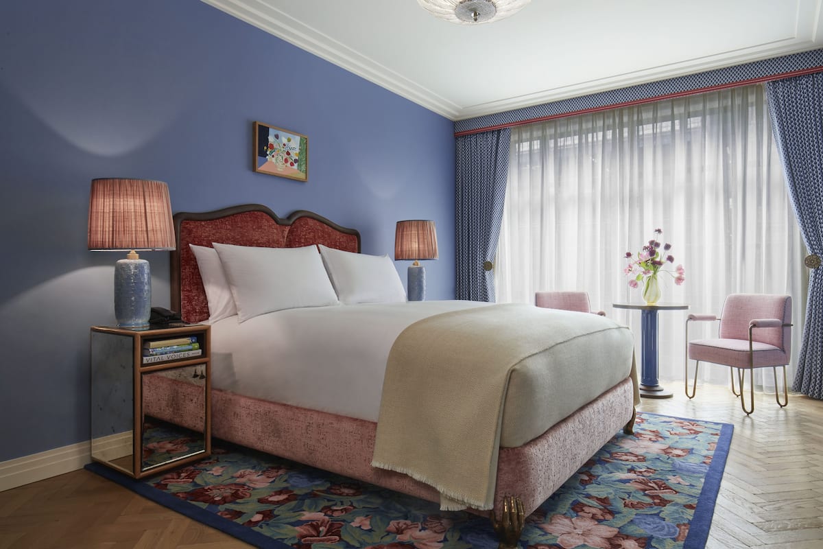 Un dormitorio con una cama, dos lámparas de noche, una mesita con un florero y una silla.