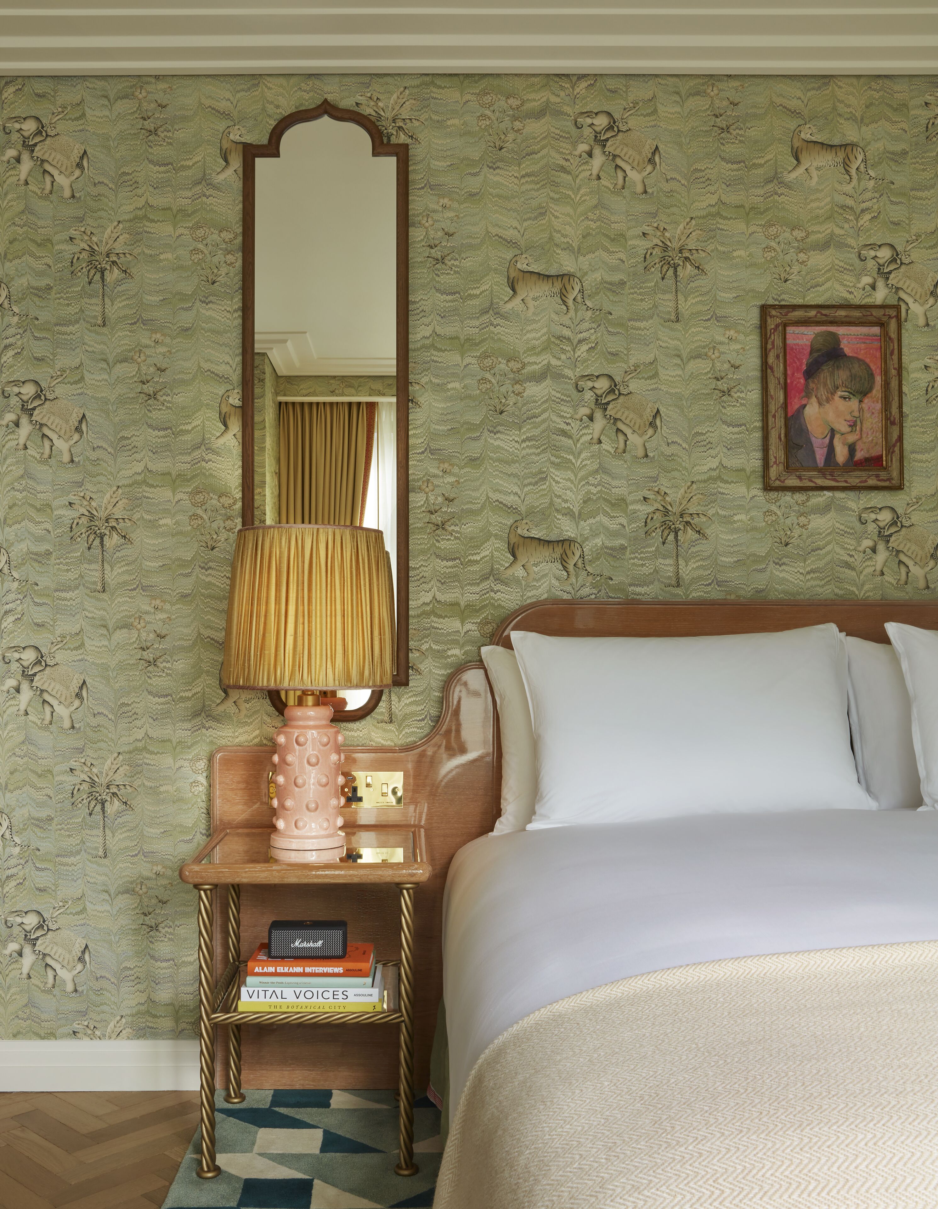 A hotel room with a bed, a nightstand with a lamp, a mirror, and a framed picture on the wall.