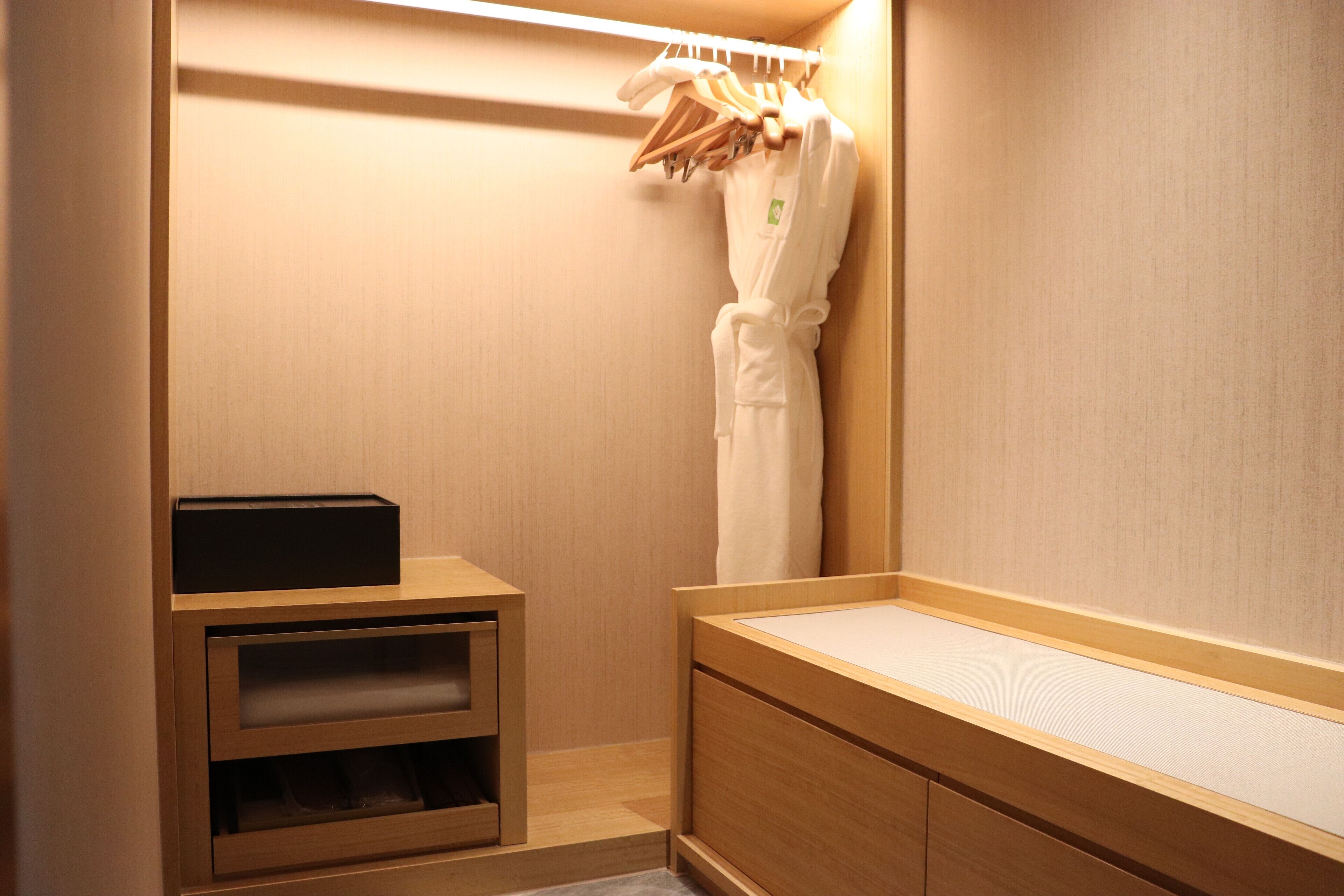 A hotel bathroom with a wooden vanity, a towel rack with robes, and a small shelf unit.