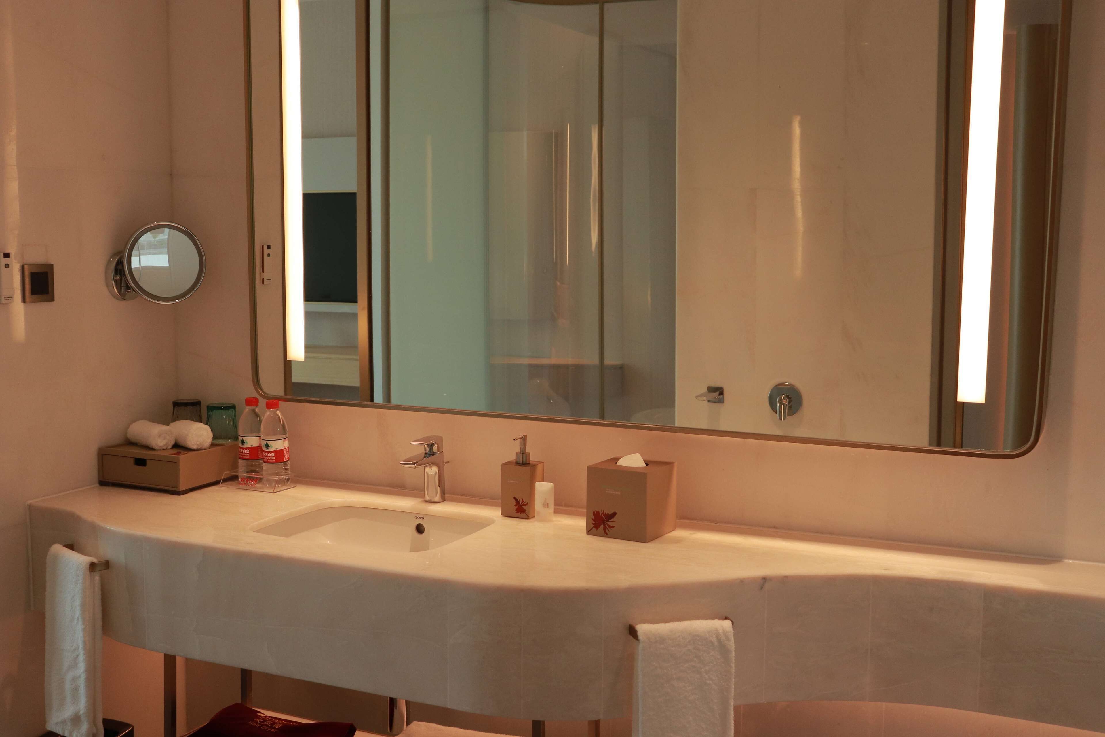 Un bagno d'albergo con uno specchio grande, un lavandino e una cabina doccia in vetro.