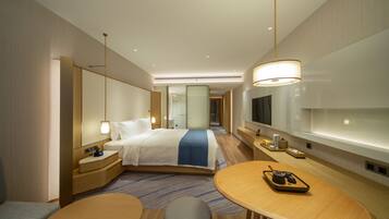 Una habitación de hotel moderna con cama, mesitas de noche, televisor y una zona de estar con mesa y sillones.
