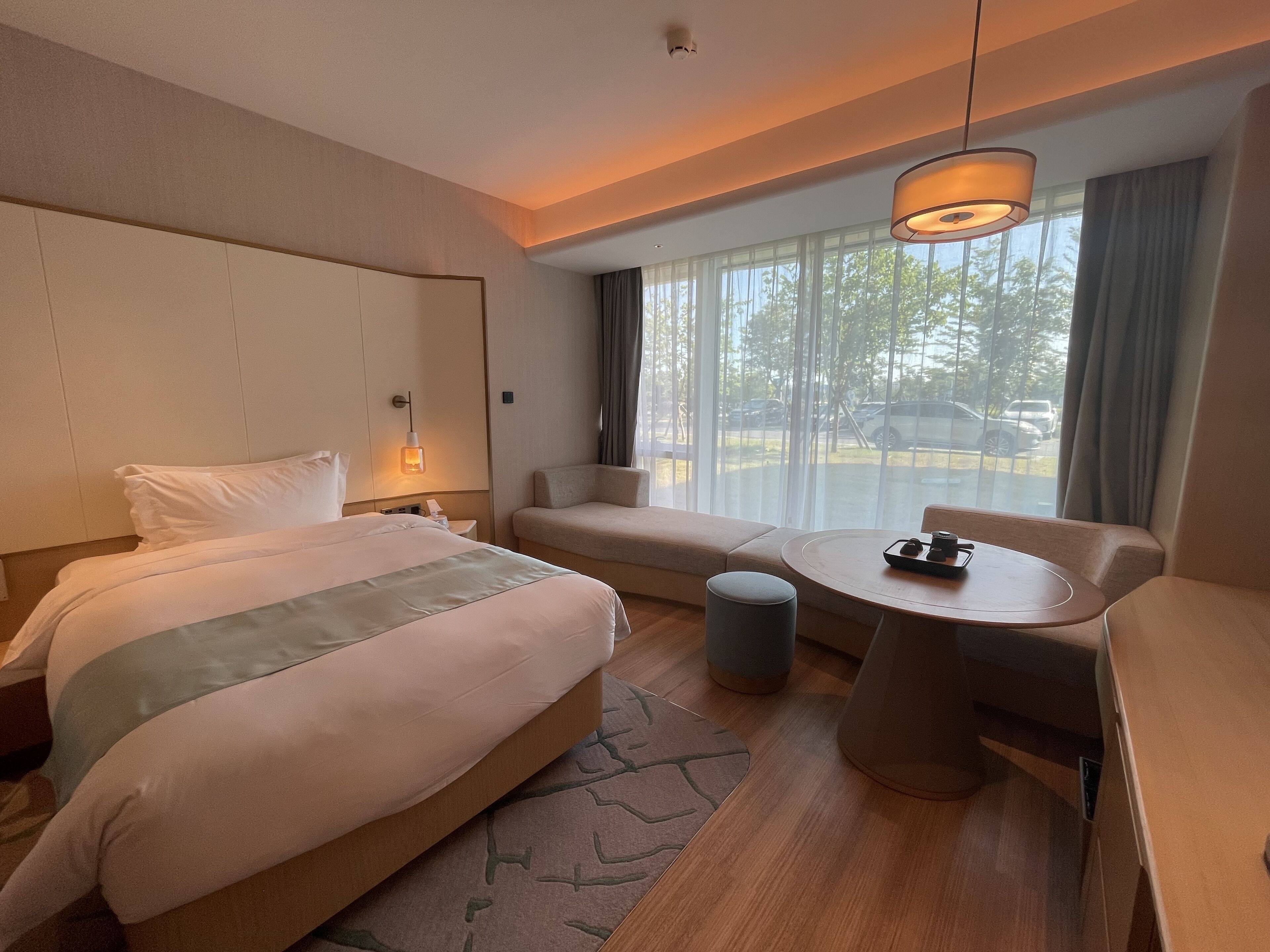 Habitación de hotel con cama, sofá, mesita y ventana con vistas al exterior.