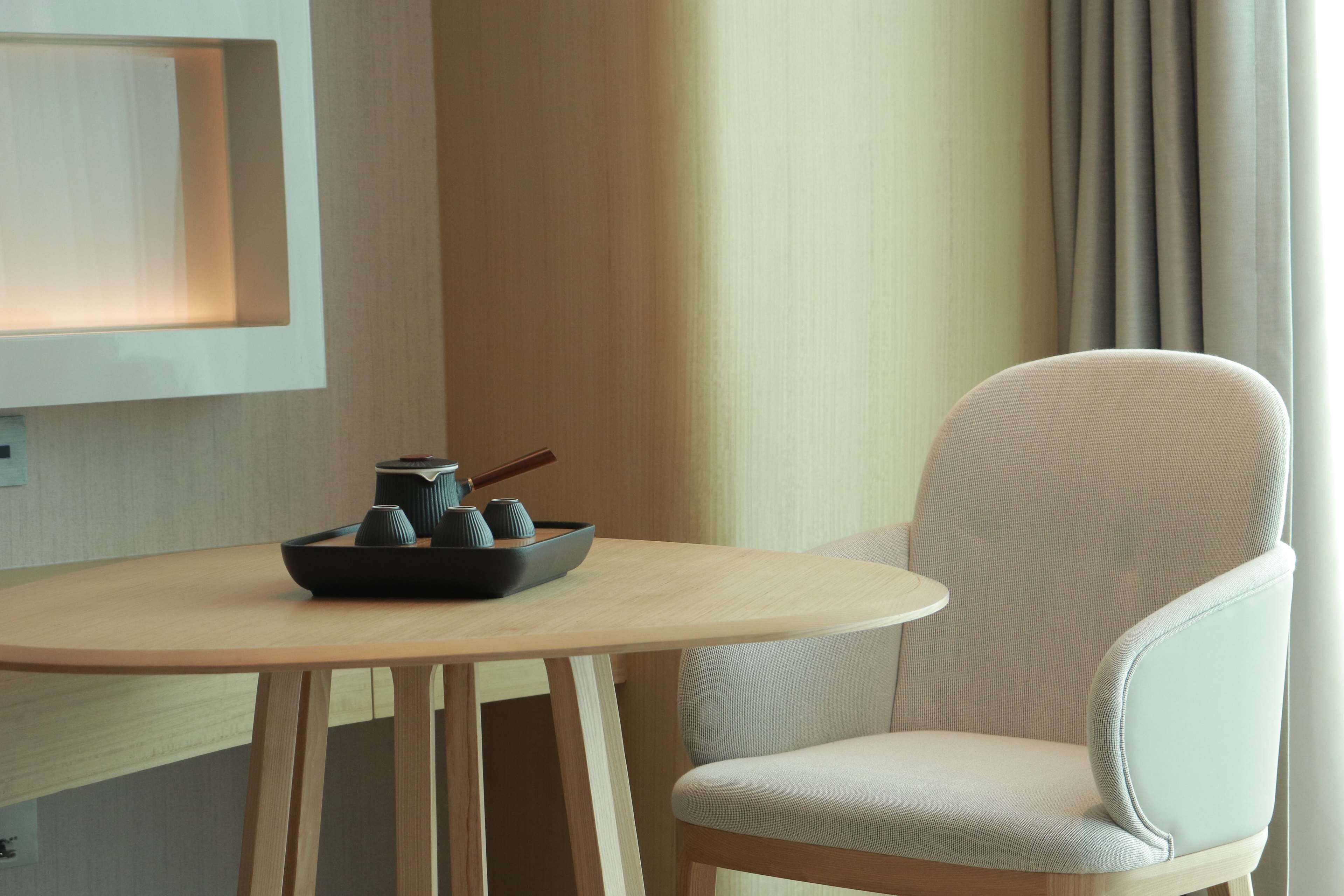 A modern hotel room with a wooden table, a chair, and a small black tray with cups and a teapot.