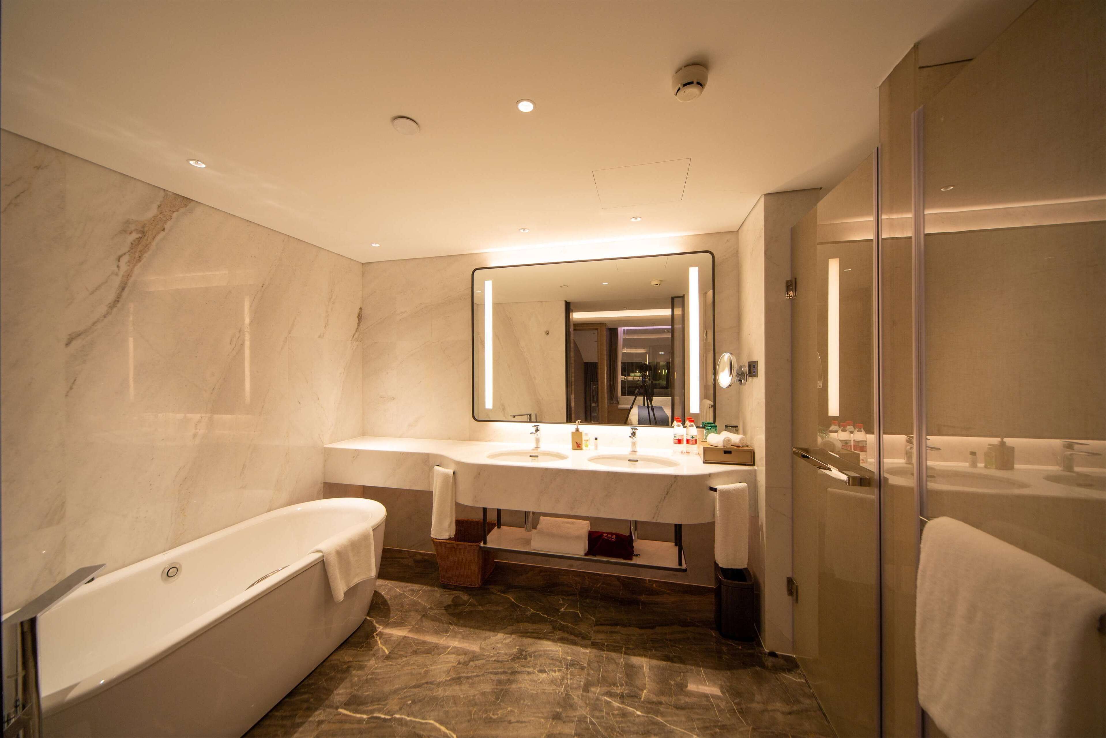 A modern bathroom with a large mirror, two sinks, a bathtub, and a shower area.