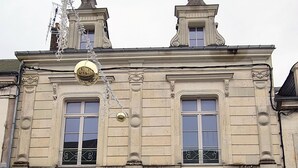 Un edificio histórico con puerta verde, dos ventanas con barandillas de hierro decorativo y un cartel de prohibido estacionar.