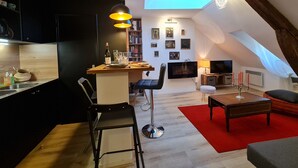 Un loft moderno con cocina, comedor y sala de estar. Cuenta con un tragaluz, un televisor de pantalla plana y una zona de estar acogedora con un tapete rojo.