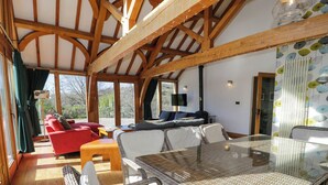 Ein geräumiger Raum mit hohen Decken, Holzbalken, einem Glastisch, Korbstühlen, einem roten Sofa und einem Fernseher.