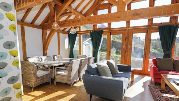 Ein geräumiges Zimmer mit Holzbalkendecke, großen Fenstern, Korbmöbeln und einem roten Sofa.