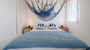 Una cama con colcha azul, dos mesitas de noche con lámparas y una hamaca colgando del techo.