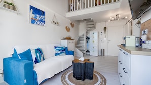 Un espacio habitable moderno con un sofá azul, una mesa de centro de madera y una escalera que conduce a una zona tipo loft.