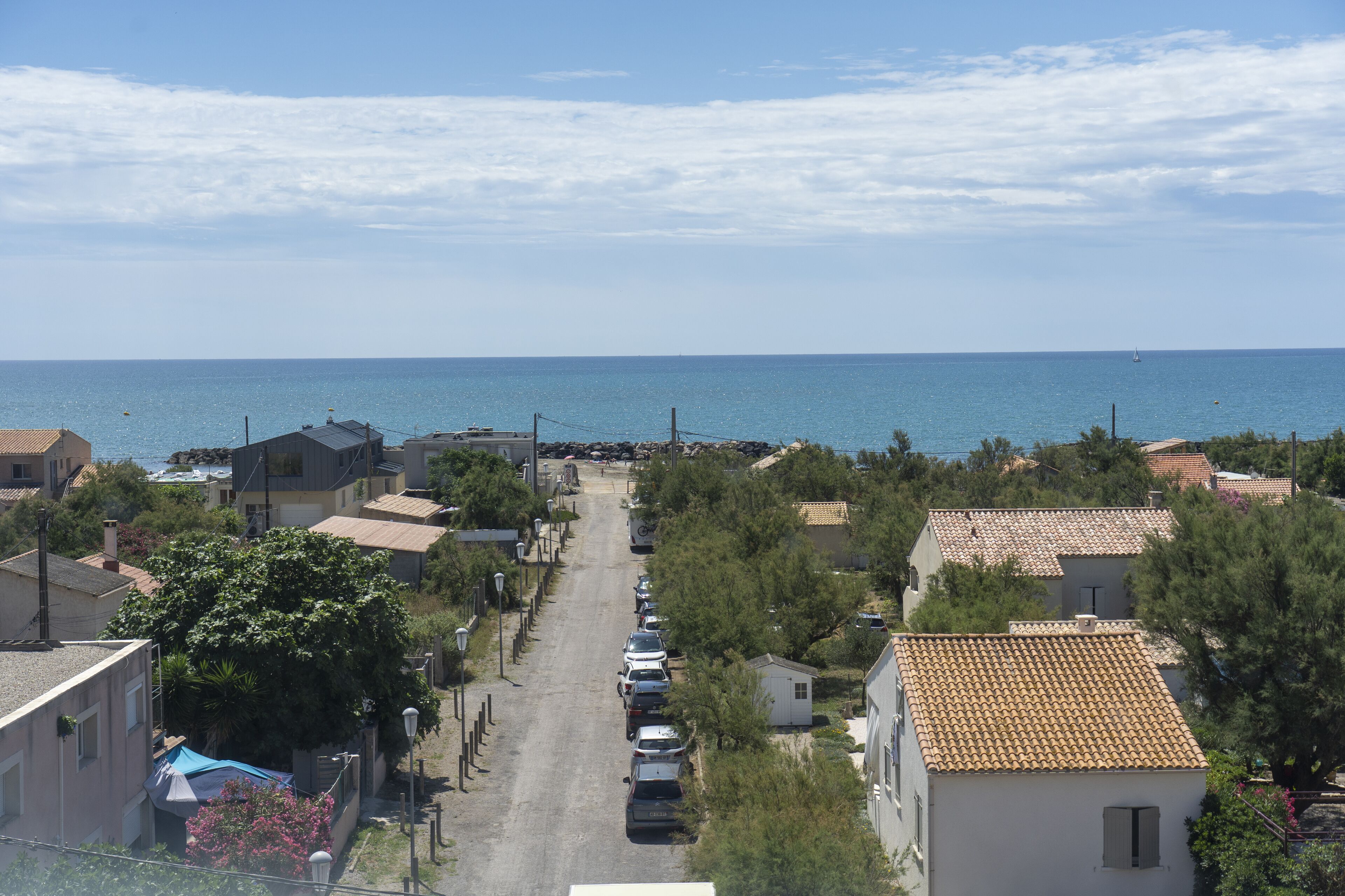 A coastal street with buildings, parked cars, and a clear view of the sea.