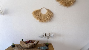 Una habitación con una mesa de madera, un cuenco de fruta, una pequeña planta en maceta y adornos en la pared, incluyendo un pez y dos diseños de rayos de sol.
