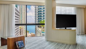 Ein modernes Hotelzimmer mit großem Fenster, Flachbildfernseher, Holztisch und einer Zeitschriftenablage.