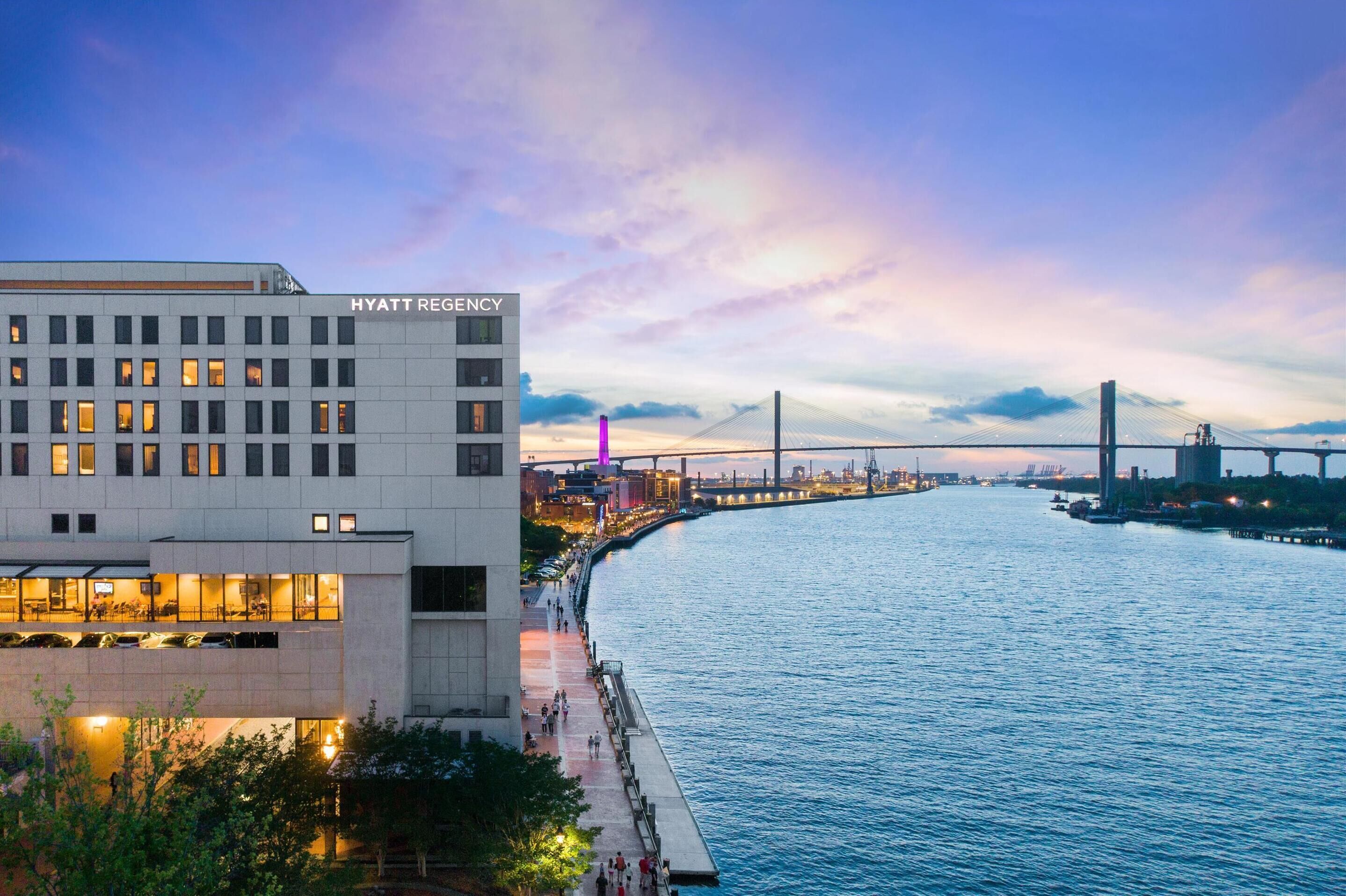 Un edificio moderno con un letrero visible de 'HYATT REGISTRY', un paseo marítimo y un puente al fondo.
