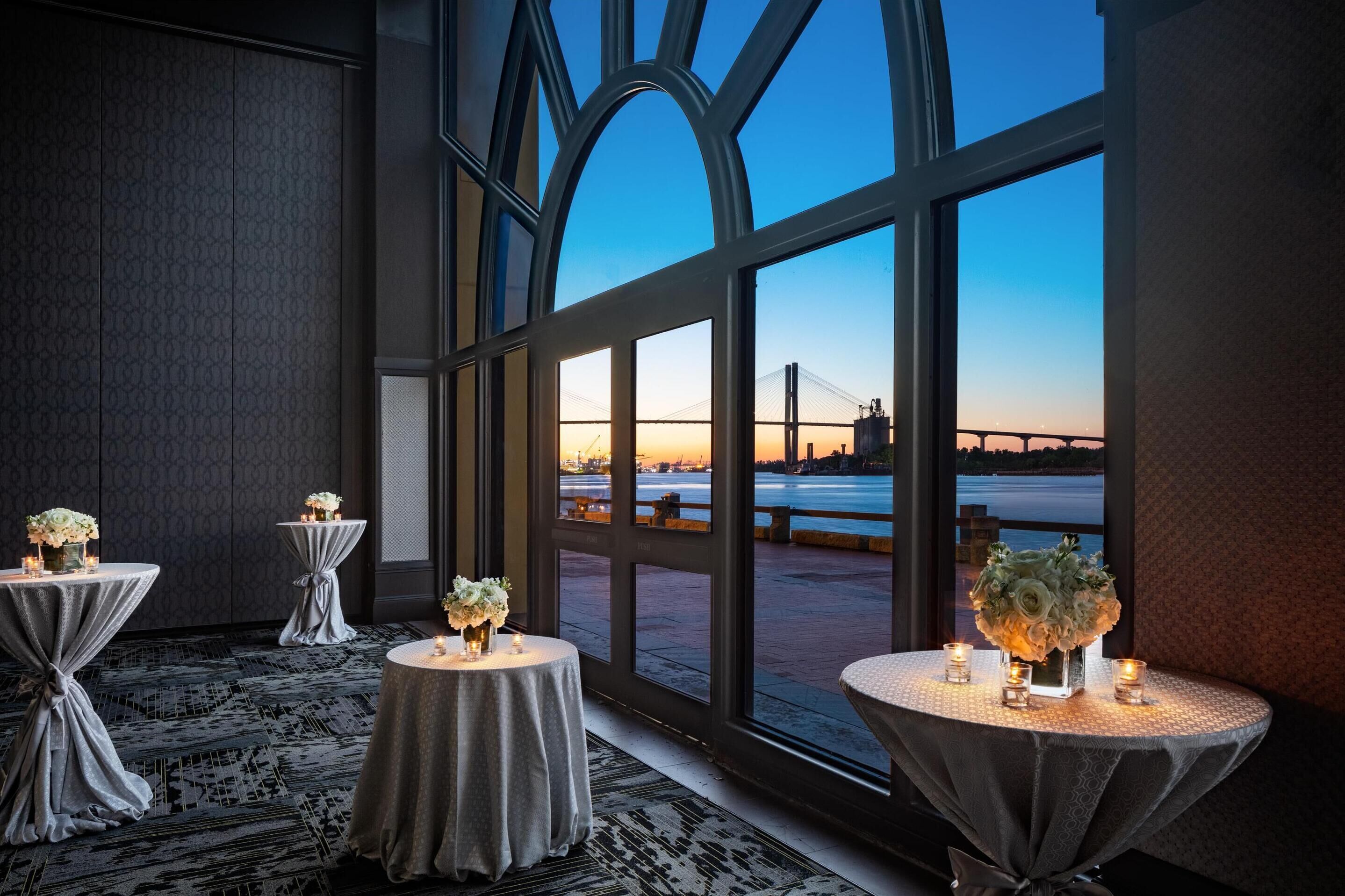 A room with large windows, tables with candles, and a view of a bridge.