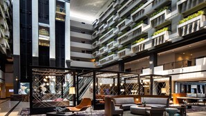 Een moderne hotellobby met een hoge plafond, meerdere verdiepingen en een centraal zithoek met banken en een salontafel.