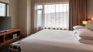 Habitación de hotel con una cama grande, un televisor sobre un soporte de madera y una ventana con cortinas.