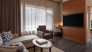 Una habitación de hotel moderna con sofá, sillón y una mesita con un libro. Hay un televisor de pantalla plana grande montado en la pared y un escritorio con una silla.
