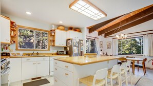 Una cocina con armarios blancos, encimera de madera y un amplio ventanal con vistas a un jardín.