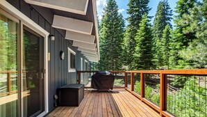 Una terraza de madera con una parrilla, un área de estar techada y vista a un área boscosa.