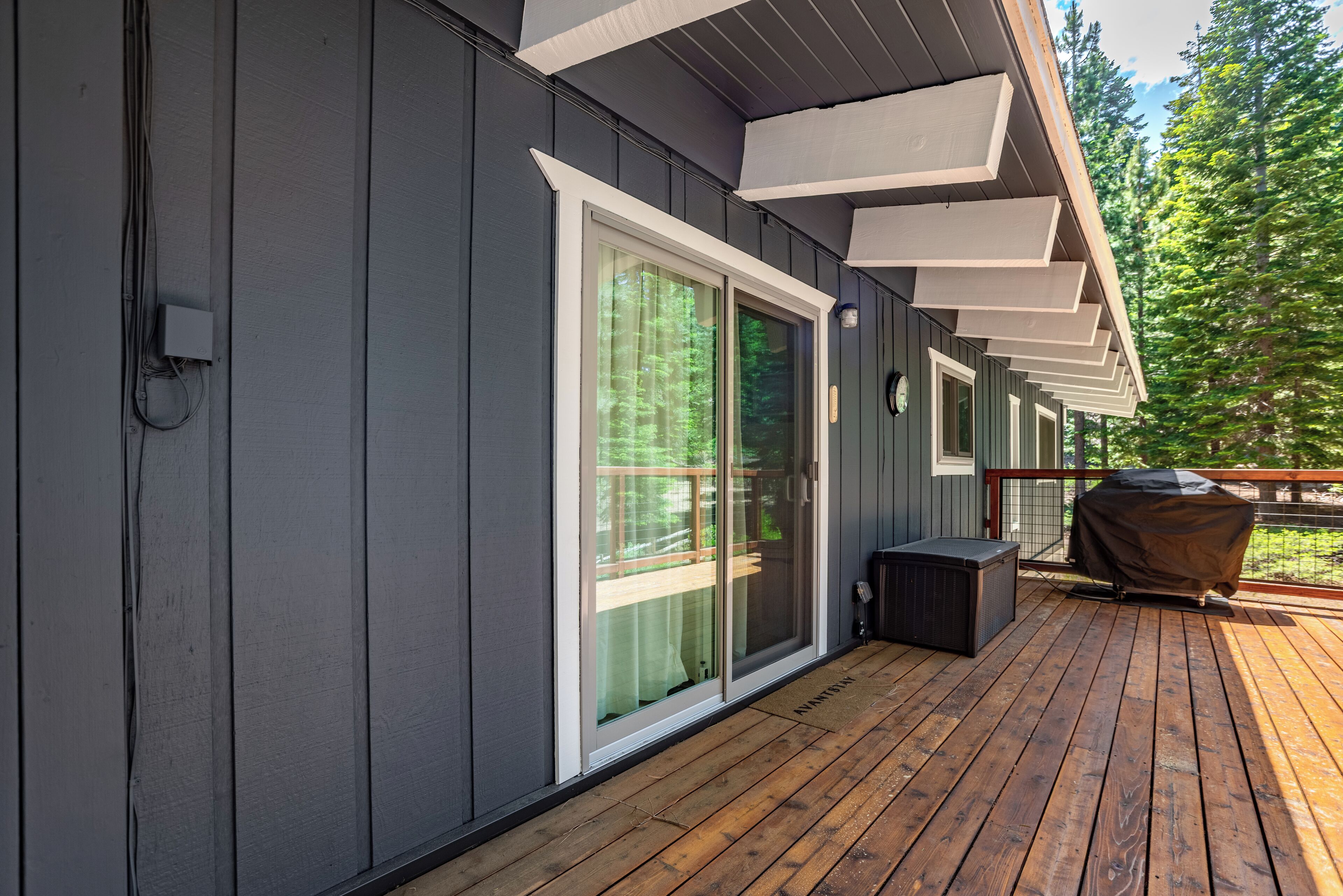 A wooden deck with a sliding glass door, a covered grill, and a power outlet on the wall.