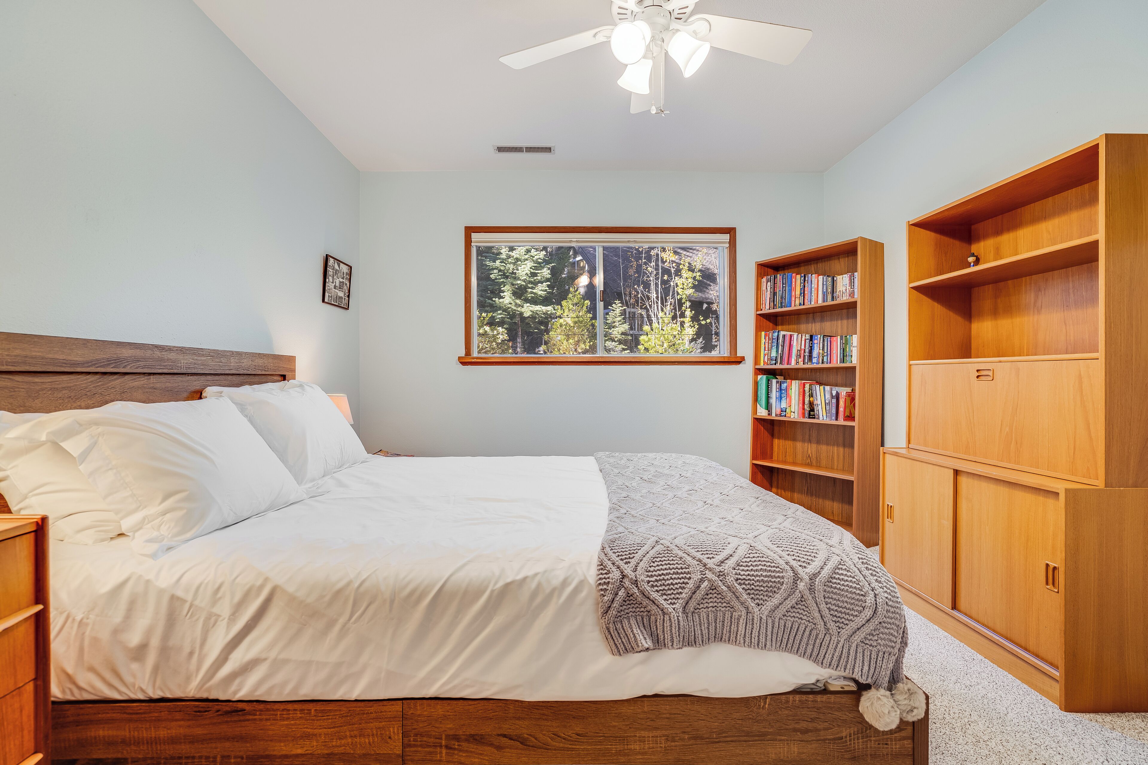 A bedroom with a wooden bed, a large window, and built-in bookshelves.
