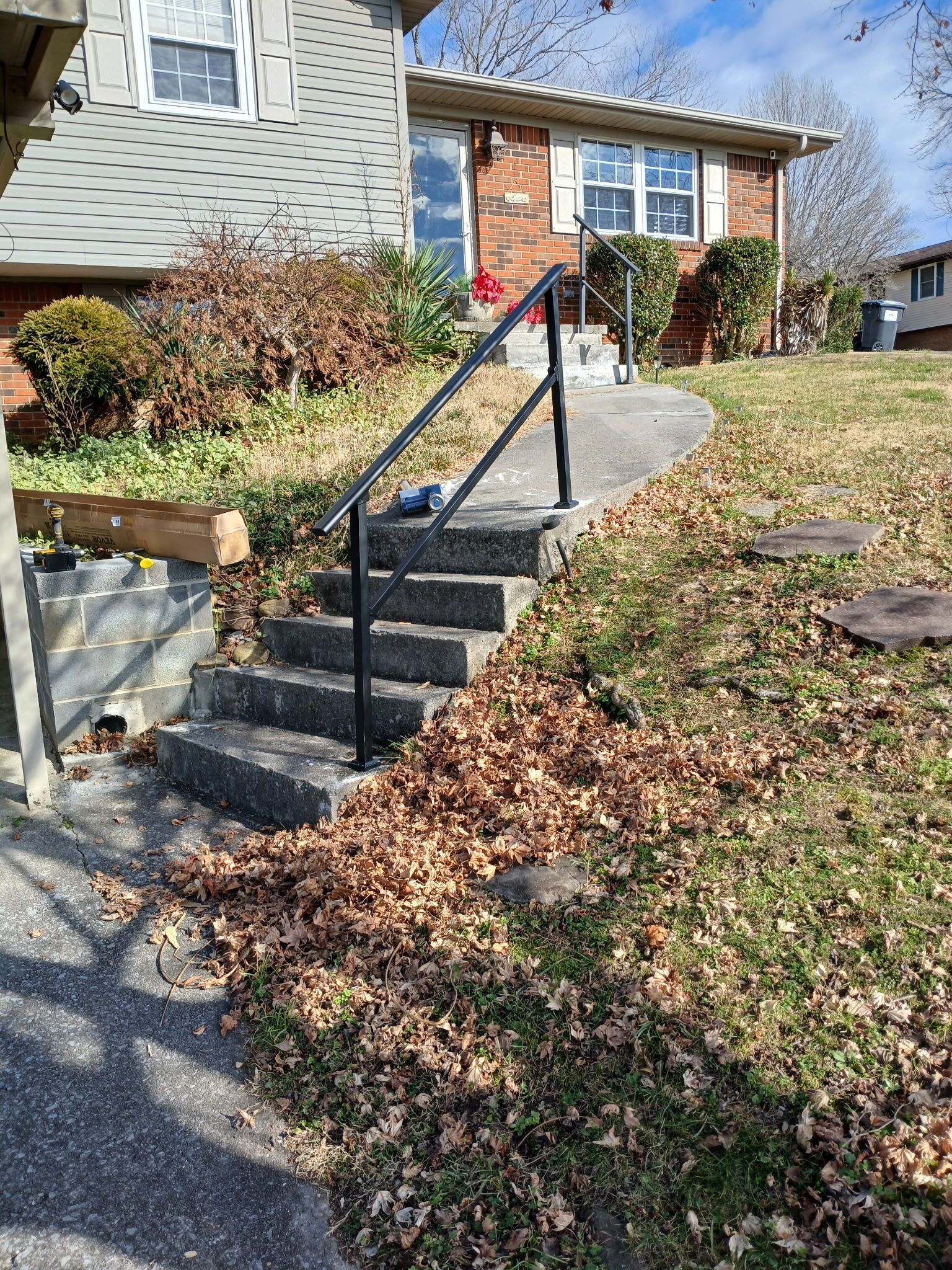 Une propriété résidentielle avec un escalier en béton menant à une maison en briques, entourée d’une pelouse jonchée de feuilles mortes.