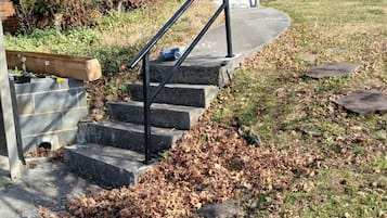 Une propriété résidentielle avec un escalier en béton menant à une maison en briques, entourée d’une pelouse jonchée de feuilles mortes.