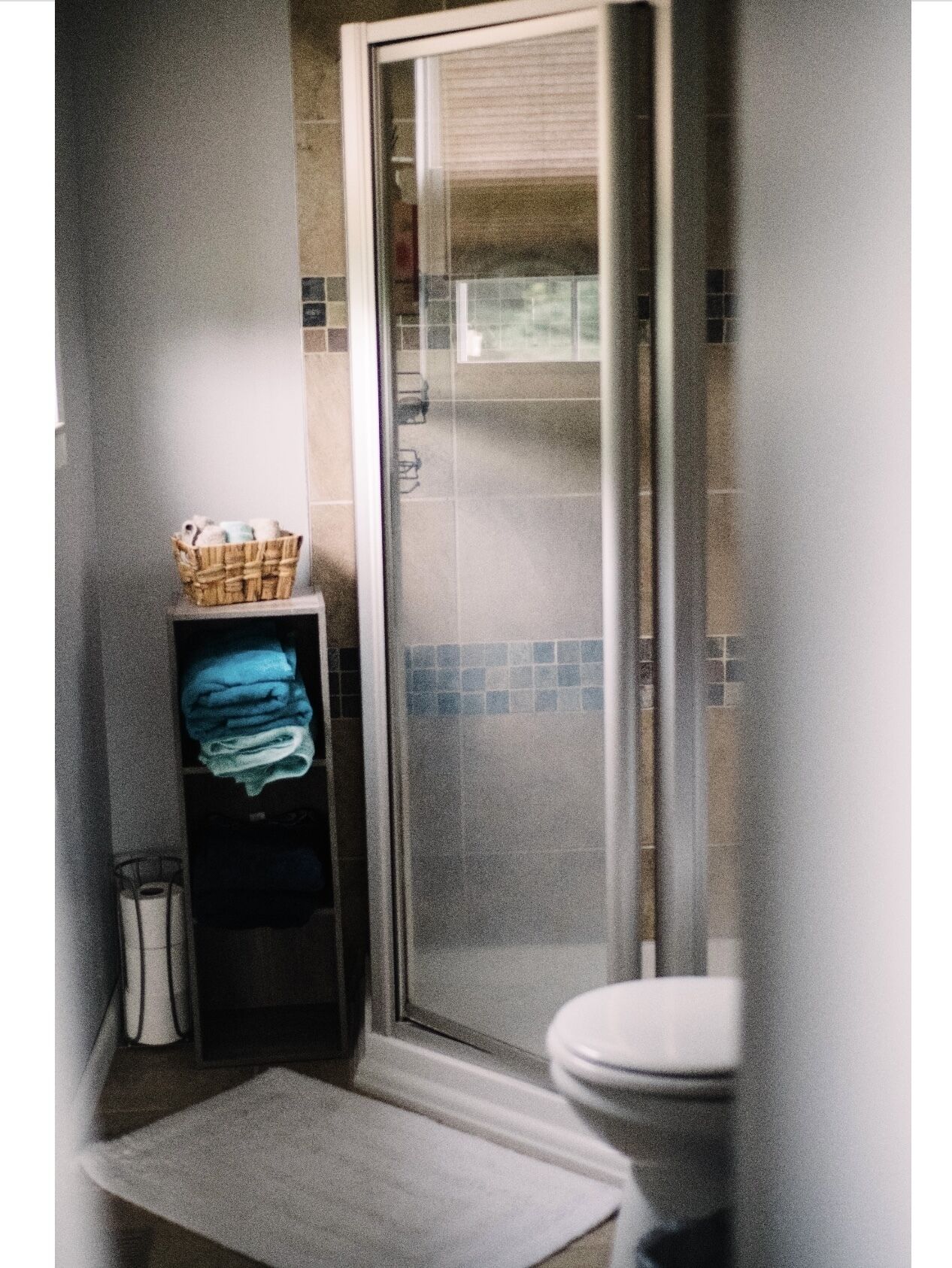 Ein Badezimmer mit Duschabtrennung aus Glas, einer Toilette, einem Handtuchhalter und einem Wäschekorb mit Handtüchern.
