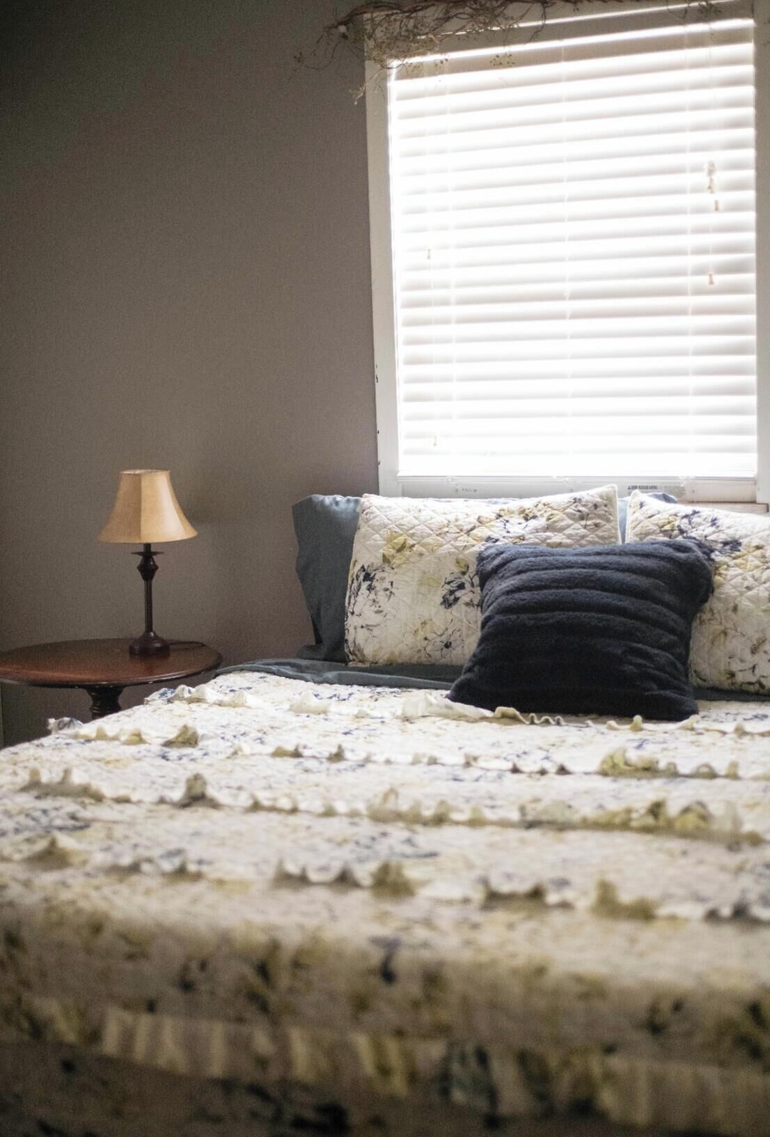A bedroom with a bed, a lamp, and a window with blinds.