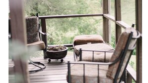 Une terrasse en bois avec deux chaises et une petite table, donnant sur un paysage verdoyant.