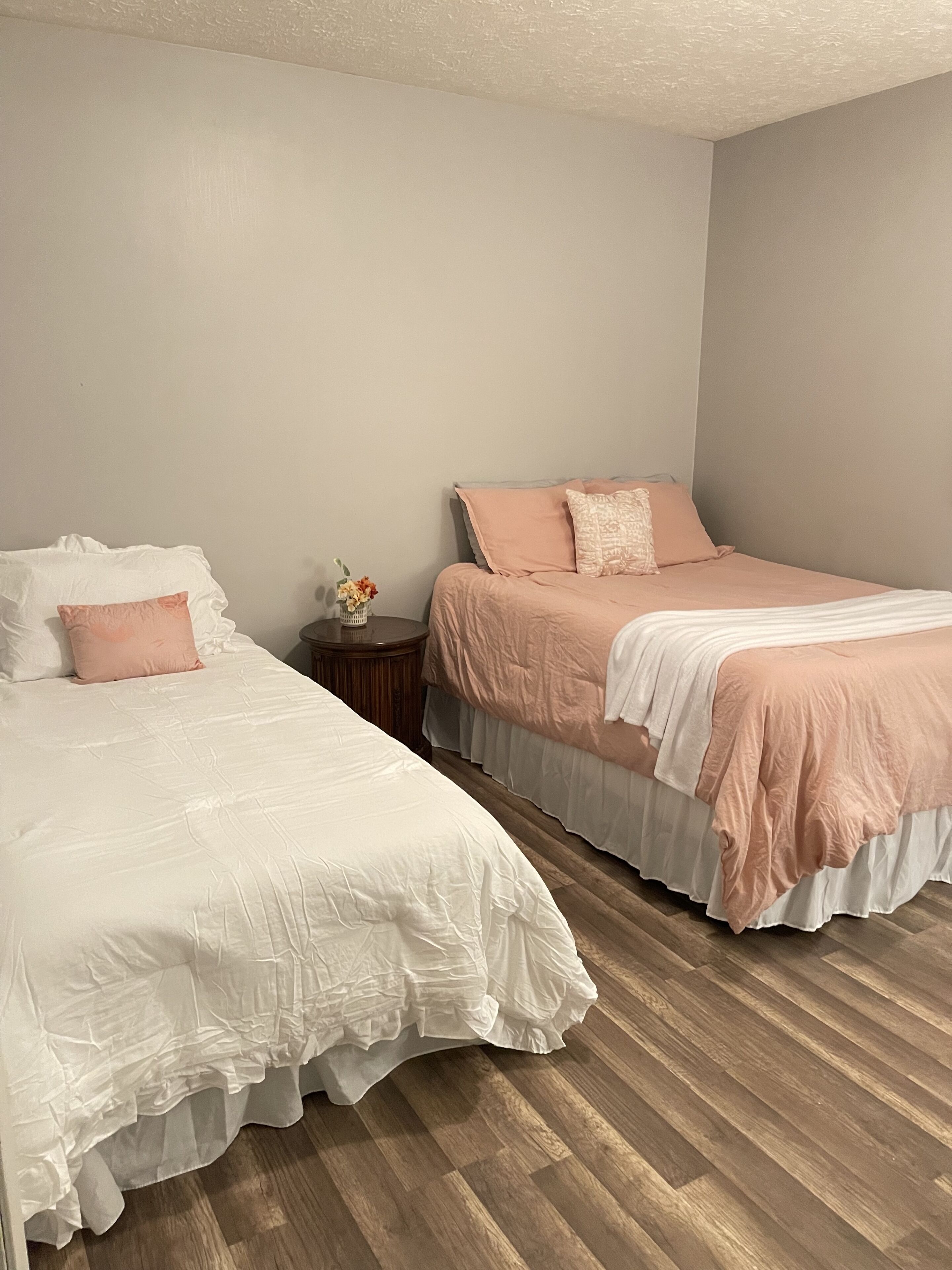 Un dormitorio con dos camas, una mesita de noche y un jarrón con flores.