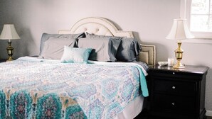 Un lit bien fait, recouvert d’une couvre-lit à motifs, avec une tête de lit à capitons et deux tables de chevet dotées de lampes.
