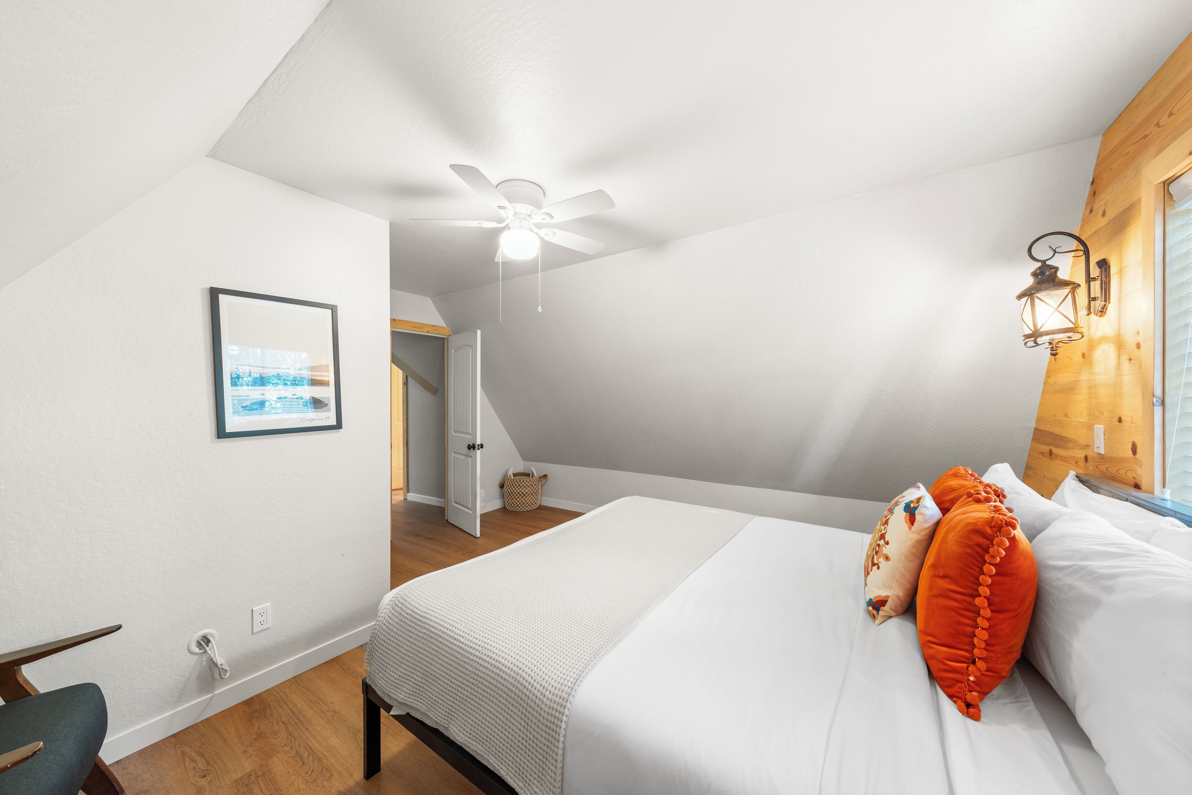Una camera da letto con un letto, una ventola a soffitto, un quadro appeso al muro e una finestra con persiane di legno.