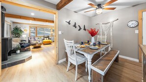 A dining area with a wooden table, white chairs, and a ceiling fan. - Hot Tub + Deck Dining • Mins to State Park Trails + Homewood Ski | Sweet Pine (Tahoma)