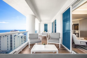 Un balcón con vista al océano, amueblado con dos sillas y una mesa, y un ventanal corredizo que da a una habitación.