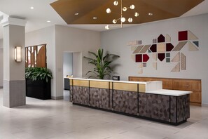 A hotel reception area with a modern design, featuring a reception desk, a large potted plant, and a wall with geometric patterns. - 2 Connecting Suites at a  Hotel (Lincoln)