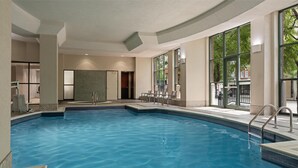 An indoor swimming pool with clear water, a tiled floor, and a seating area with chairs and tables. - 2 Connecting Suites at a  Hotel (Lincoln)