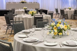 A banquet hall with round tables set for dining, each with plates, cutlery, and glasses.