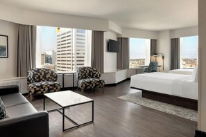 A hotel room with a bed, two armchairs, a small table, a TV, and a view of the cityscape. - 2 Connecting Suites at a 4⭐️ Hotel (Seattle)