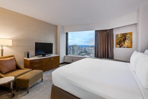 A hotel room with a bed, a TV, a desk, a chair, and a window with a city view.