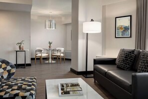 A modern living room with a black leather sofa, a patterned armchair, a coffee table with a magazine, a floor lamp, and a dining area with a table and chairs. - 2 Connecting Suites at a 4⭐️ Hotel (Seattle)