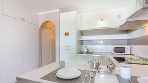 A modern kitchen with white cabinets, a microwave, and a dining area with a table set for two. - Spectacular apartment with sunset ocean views in Fanabe Beach with free WIFI (Costa Adeje)