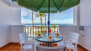 A balcony with a table and chairs, a green umbrella, and a view of the sea and palm trees. - Spectacular apartment with sunset ocean views in Fanabe Beach with free WIFI (Costa Adeje)