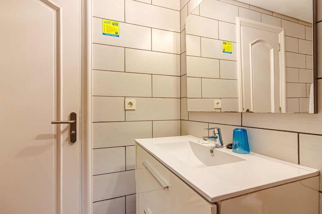 A bathroom with white tiles, a sink, a mirror, and a door.