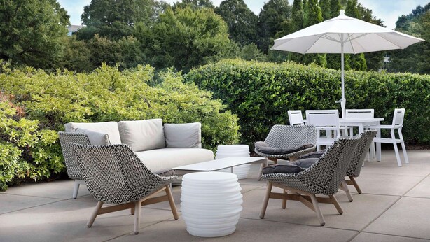An outdoor patio with a white sofa, patterned chairs, a white table, and a large umbrella. - 2 Connecting Suites at a  Hotel (Kennesaw)