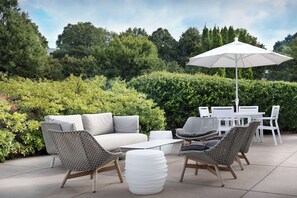 Eine Terrasse im Freien mit einem weißen Sofa, gemusterten Stühlen, einem weißen Tisch und einem großen Sonnenschirm.