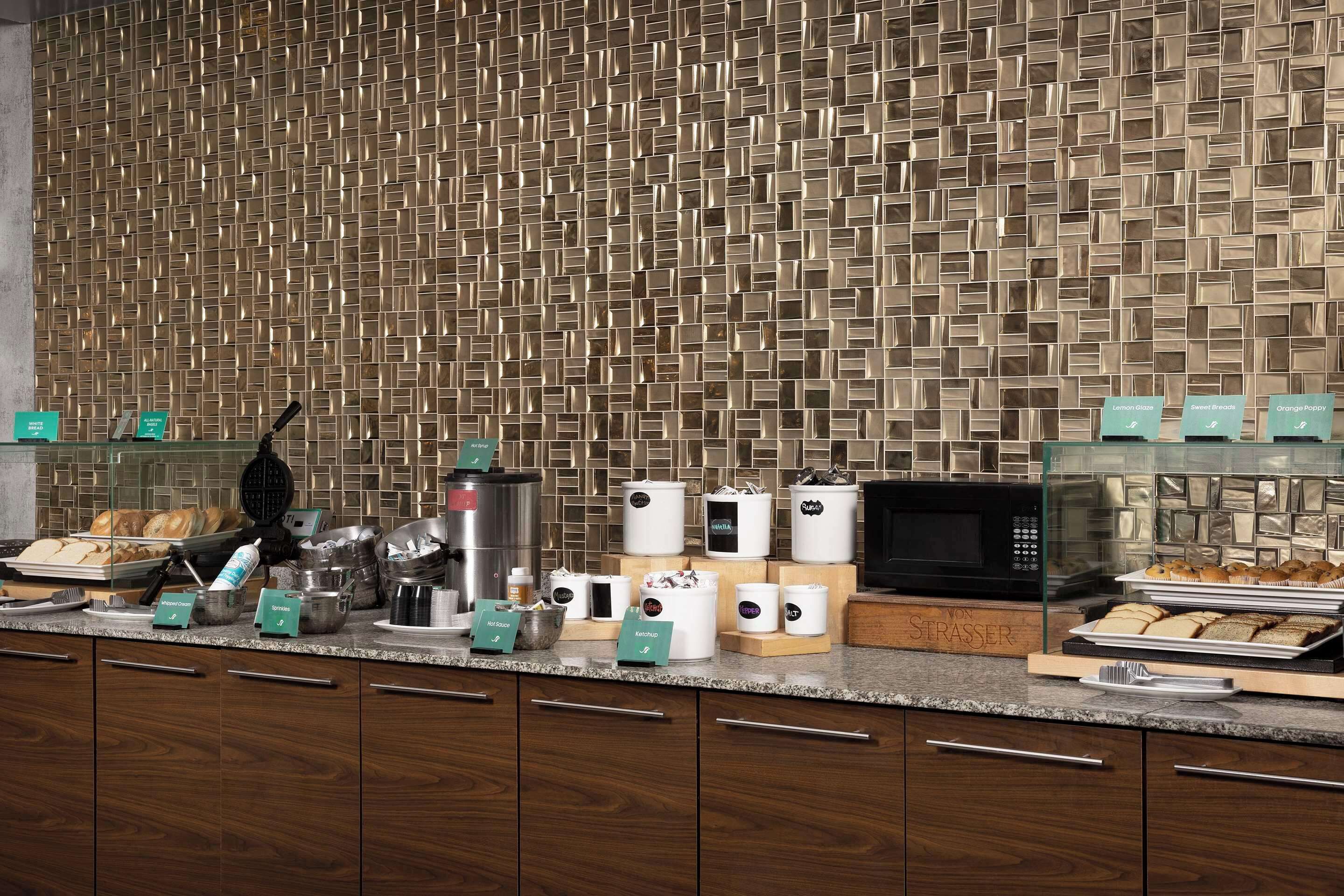 A hotel kitchen with a patterned backsplash, various kitchen appliances, and a buffet setup.